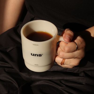 This photograph captures a serene still life, focusing on a minimalist ceramic mug set against a deep, contrasting dark textile. The visual language emphasizes quiet sophistication through the juxtaposition of smooth ceramic texture and matte fabric, creating an intimate and refined atmosphere.