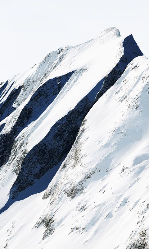 This image showcases a dramatic alpine landscape defined by stark contrasts between brilliant white snow and deep indigo shadows. The visual language emphasizes texture, depth, and the harsh beauty of high-altitude environments through masterful use of light and shadow.