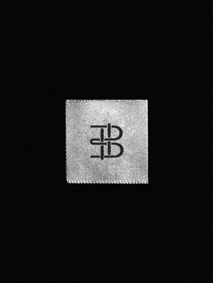 This is a minimalist design featuring a subtle, textured patch or label against a stark black background. The visual language relies on high contrast and simple geometric forms to create a clean, enduring brand mark.