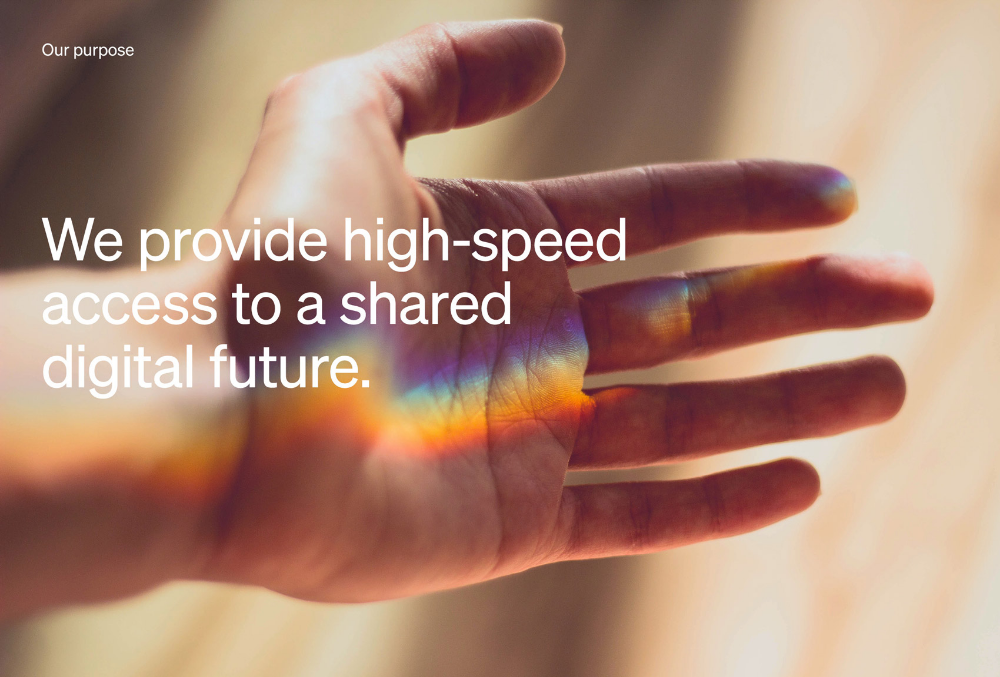 This image utilizes macro photography of a hand to visually bridge the gap between the physical and digital realms, using light refraction to create vibrant spectral gradients across the skin. The design effectively uses organic textures and warm tones to convey a message about future technology and shared access.