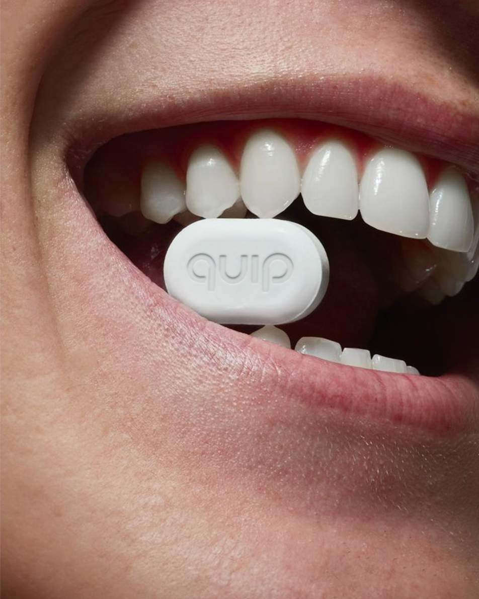 This is a macro photograph showcasing a small, white product against the natural texture of human teeth and skin. The visual language is clean and bright, emphasizing purity and clinical functionality through tight framing.