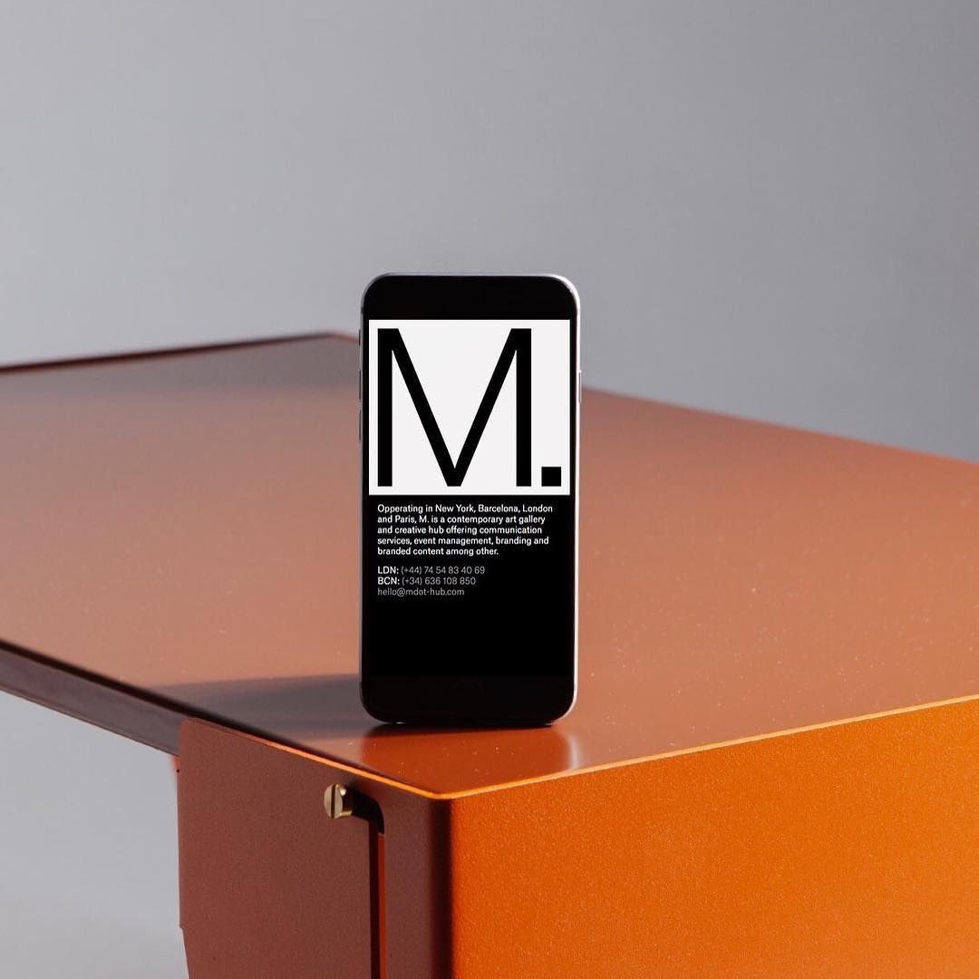 The image features a minimalist presentation of a smartphone displaying a large, stark monogram against a warm, matte surface. The design emphasizes clean lines, negative space, and a sophisticated, modern aesthetic.