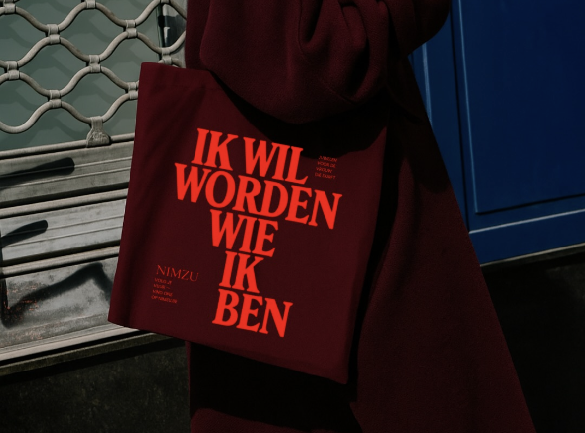 This image features a striking study in color and texture, pairing a deep, matte garment with a bold graphic print on a tote bag. The visual language combines industrial grit, evident in the metal grate and dark surfaces, with assertive typography to create a powerful statement.