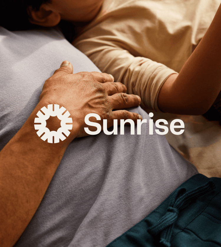 A warm, intimate lifestyle photograph featuring two people in close physical contact, overlaid with the 'Sunrise' brand mark and sans-serif typography. The image conveys human connection and comfort through natural lighting and soft, neutral tones. The design balances documentary photography with clean, modern branding elements.