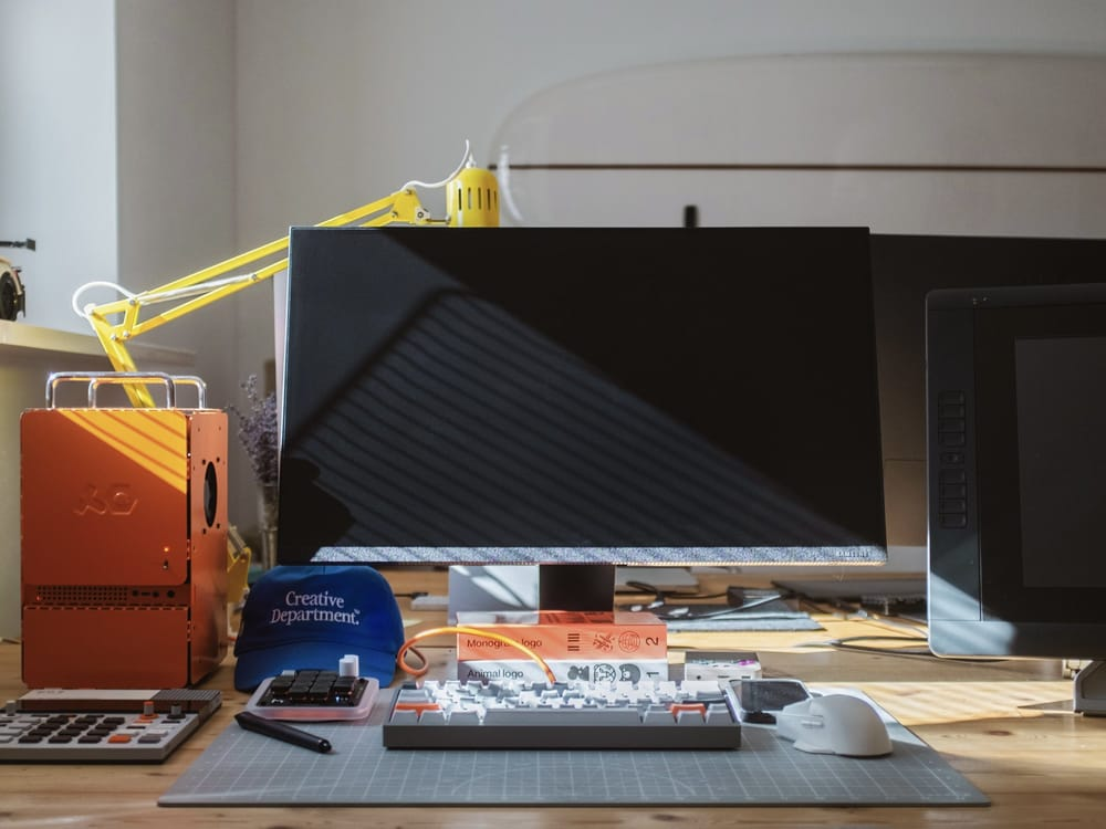 This image captures a focused, modern workspace dedicated to technical work, featuring a large monitor and various electronic components arranged on a wooden surface. The visual language emphasizes functionality and a clean, organized aesthetic, highlighting the intersection of hardware and creative endeavor.