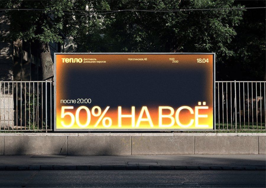 A bold outdoor advertisement billboard featuring a striking gradient from dark navy to vibrant orange-yellow, with large Cyrillic text promoting a 50% discount. The design uses high contrast and luminous typography against a dark background, creating an eye-catching commercial display mounted on a street barrier with natural foliage visible above.