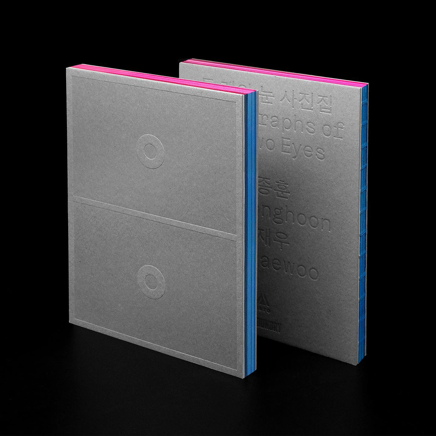 This design showcases a minimalist approach, utilizing stark contrast between matte gray surfaces and vibrant pink accents to create visual interest. The composition emphasizes clean lines, precise typography, and the tactile quality of the paper stock against a dark background.