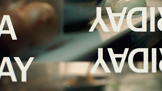 The image features a close-up, slightly blurred view of text overlaid on what appears to be a glass or reflective surface. The design is minimalist and modern, relying on negative space and clean typography to convey a sense of announcement or celebration.