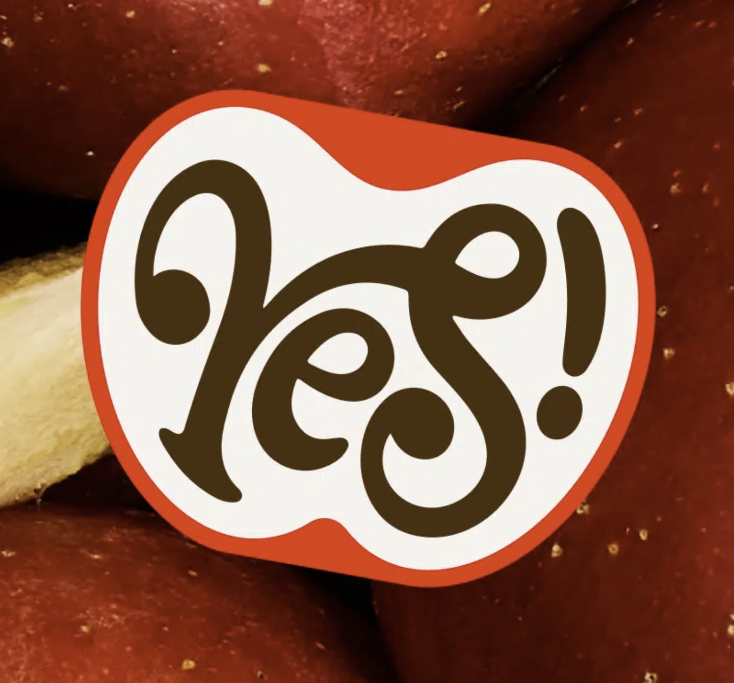 This image combines rich organic texture with a clean, illustrative graphic to create an inviting visual. The design utilizes high contrast between the deep tones of the fruit and a bright label to emphasize a simple, affirmative message. The overall feel is warm, artisanal, and naturally appealing.