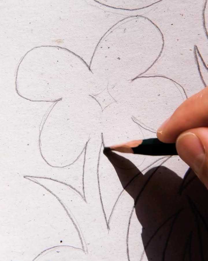 This is a close-up study of a hand drawing a simple, organic floral motif on white paper. The visual language is minimalist and sketchy, focusing on line quality and negative space to create a delicate, hand-drawn aesthetic.