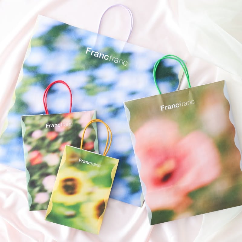This image showcases a collection of branded paper bags, likely for a company named 'Francfranc', featuring soft, nature-inspired color palettes and organic imagery. The design emphasizes a light, airy, and natural aesthetic suitable for lifestyle or retail products.