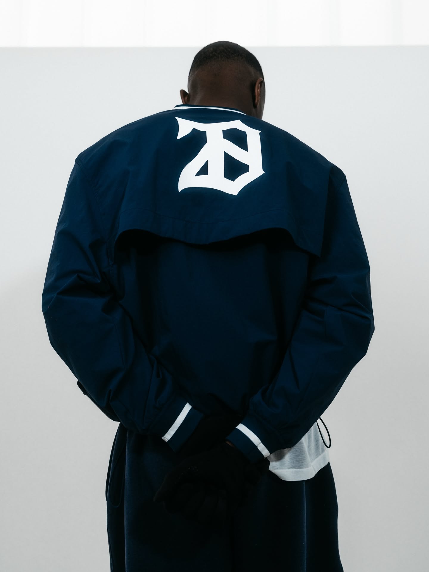 This image captures a minimalist study of dark outerwear, highlighting the structure and branding on the back of the garment. The visual language emphasizes clean lines, high contrast between the navy fabric and the white lettering, conveying a strong yet understated athletic aesthetic.