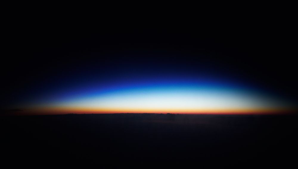 This image captures a striking atmospheric gradient, showcasing the subtle transition of light across the horizon. The visual language relies heavily on smooth tonal shifts and deep contrasts between the dark silhouette and the vibrant sky hues. The overall feel is one of vastness, serenity, and the ephemeral beauty of twilight.