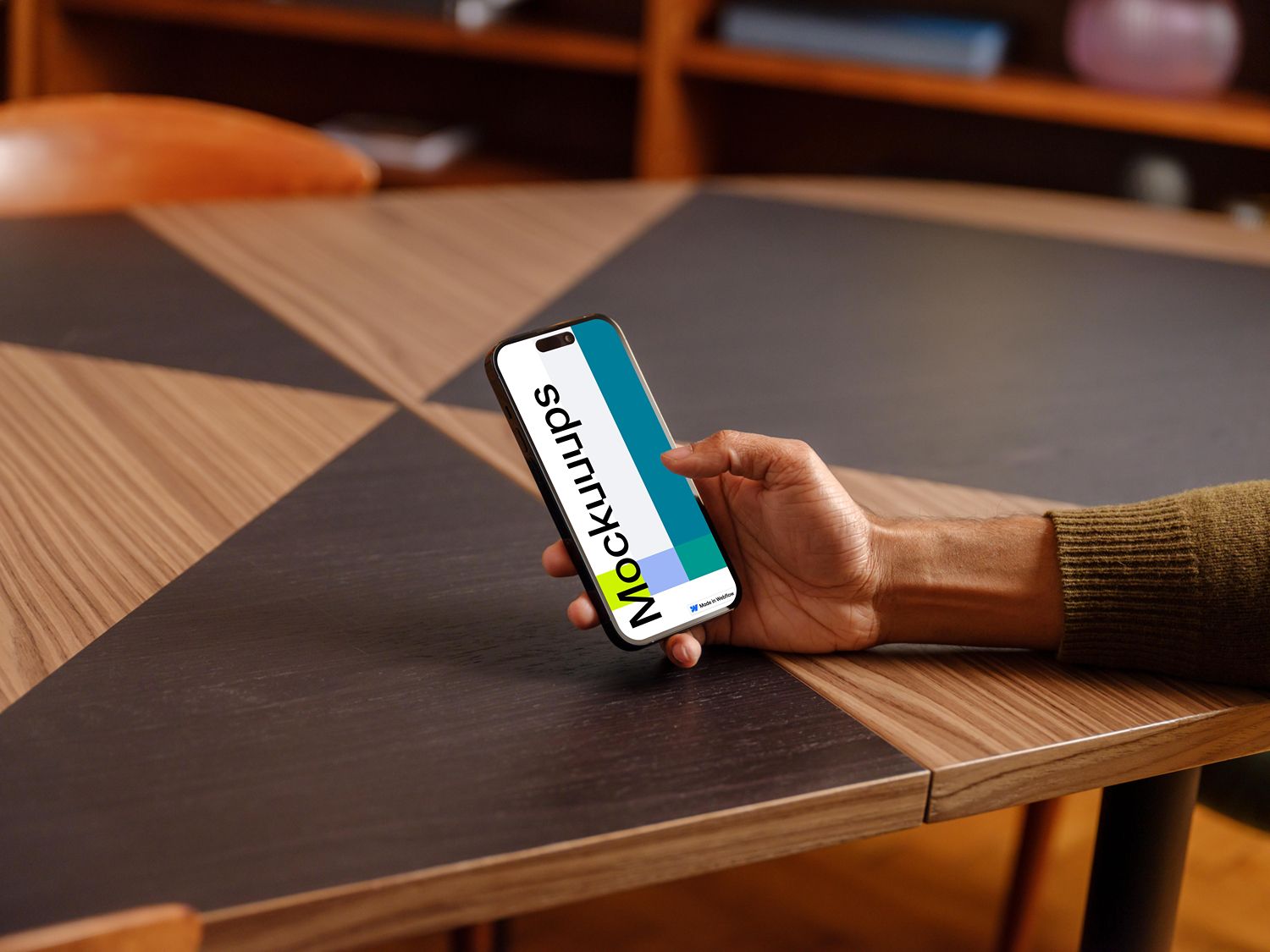 A minimalist product mockup featuring a smartphone held in a hand against a modern wooden desk with geometric surface patterns. The design emphasizes clean lines, natural materials, and contemporary workspace aesthetics with warm, professional lighting.