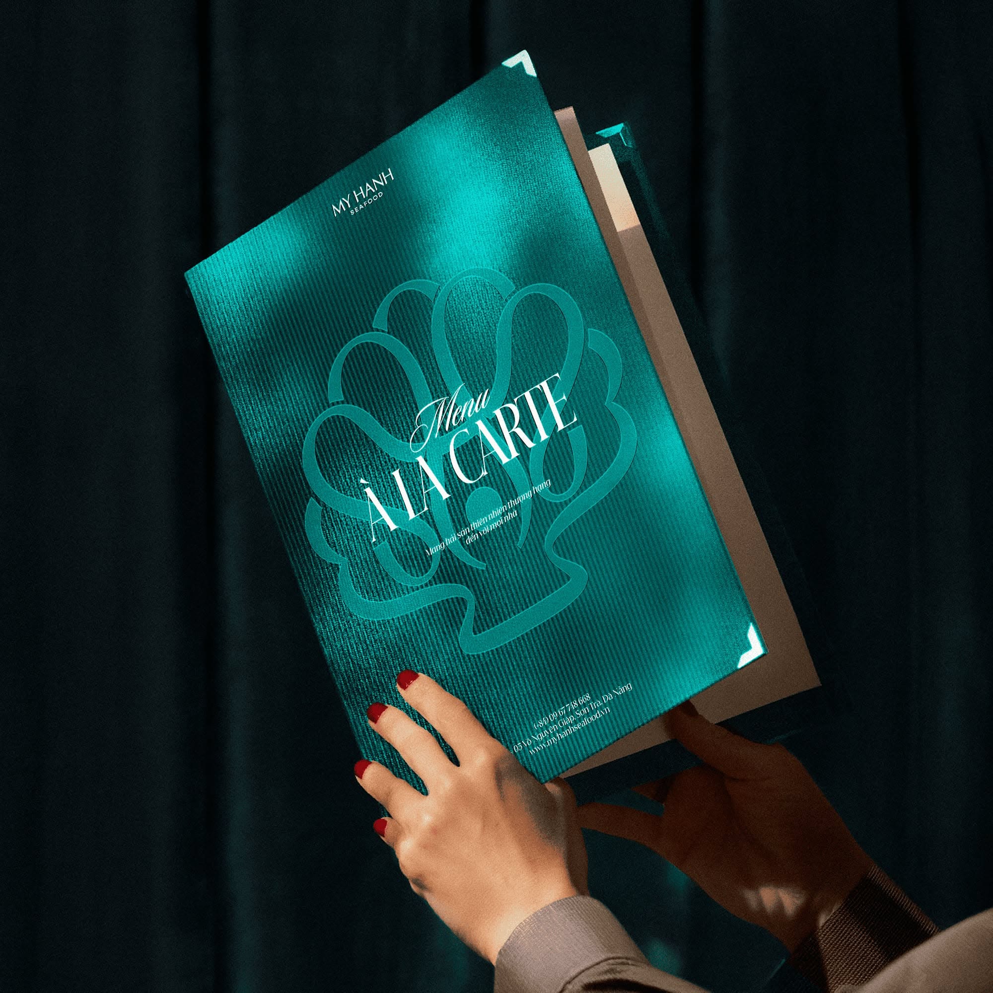 The image features a close-up of a menu cover, characterized by a vibrant teal background and an embossed or stylized graphic element. The design conveys a sense of elegance, freshness, and artisanal quality through its clean lines and focused typography.