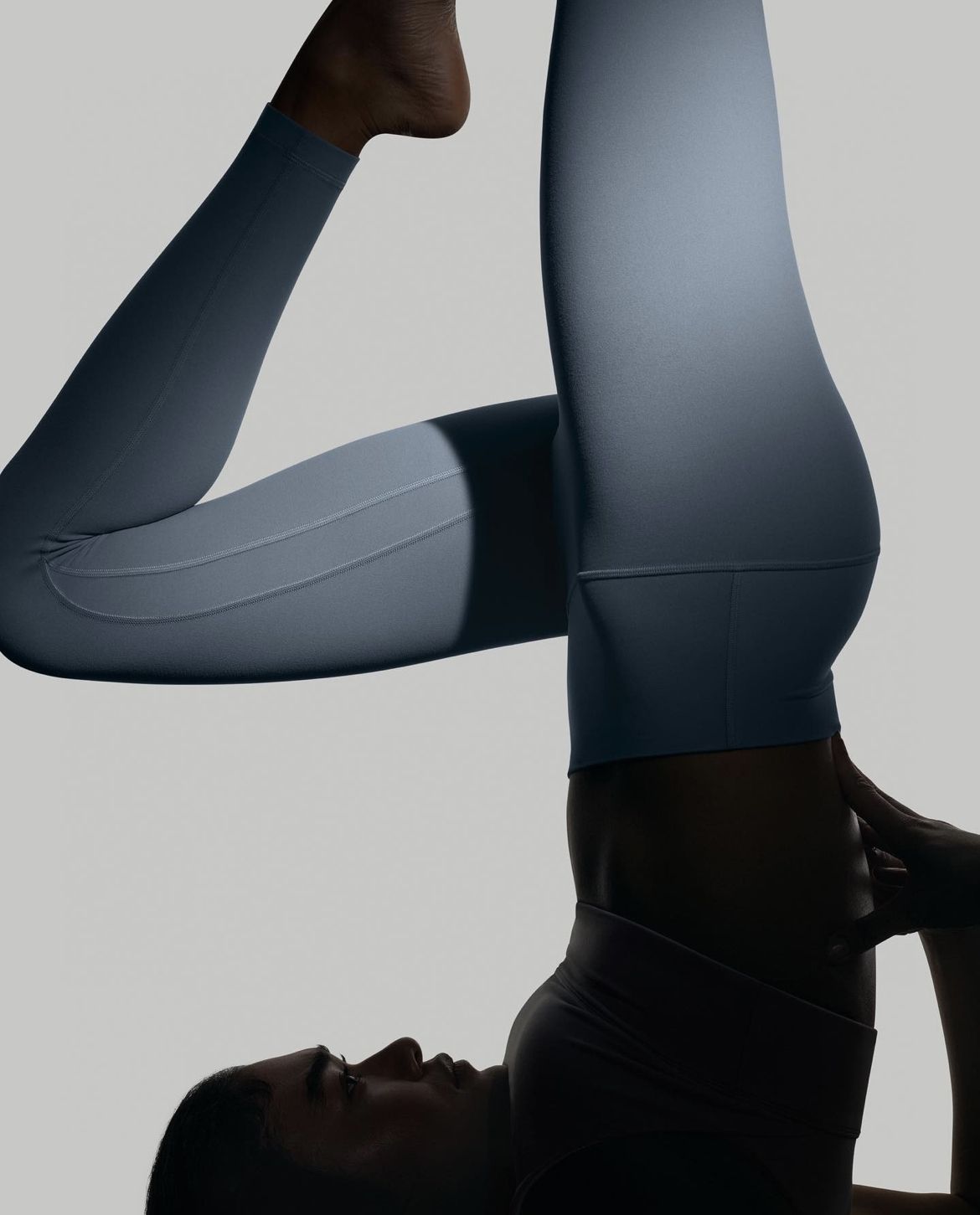 This image showcases a clean, minimalist study of human form and movement, utilizing soft studio lighting to define the contours of athletic wear. The visual language relies on smooth gradients and high contrast between light surfaces and deep shadows to emphasize silhouette and texture.