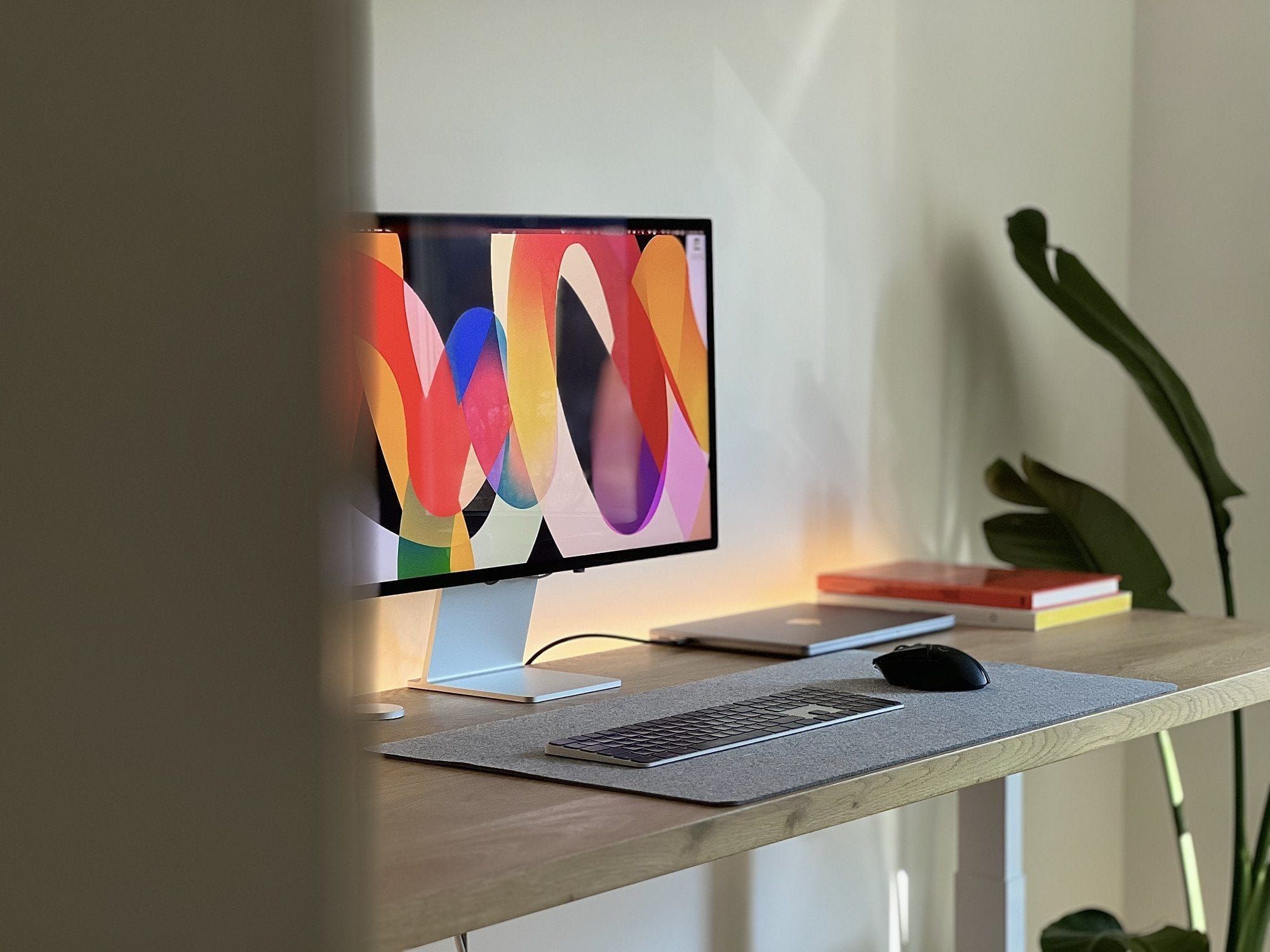 This image captures a modern, minimalist workspace setup featuring a vibrant abstract artwork displayed on a monitor. The design emphasizes clean lines, natural wood tones, and soft lighting, creating a calm yet visually stimulating environment.
