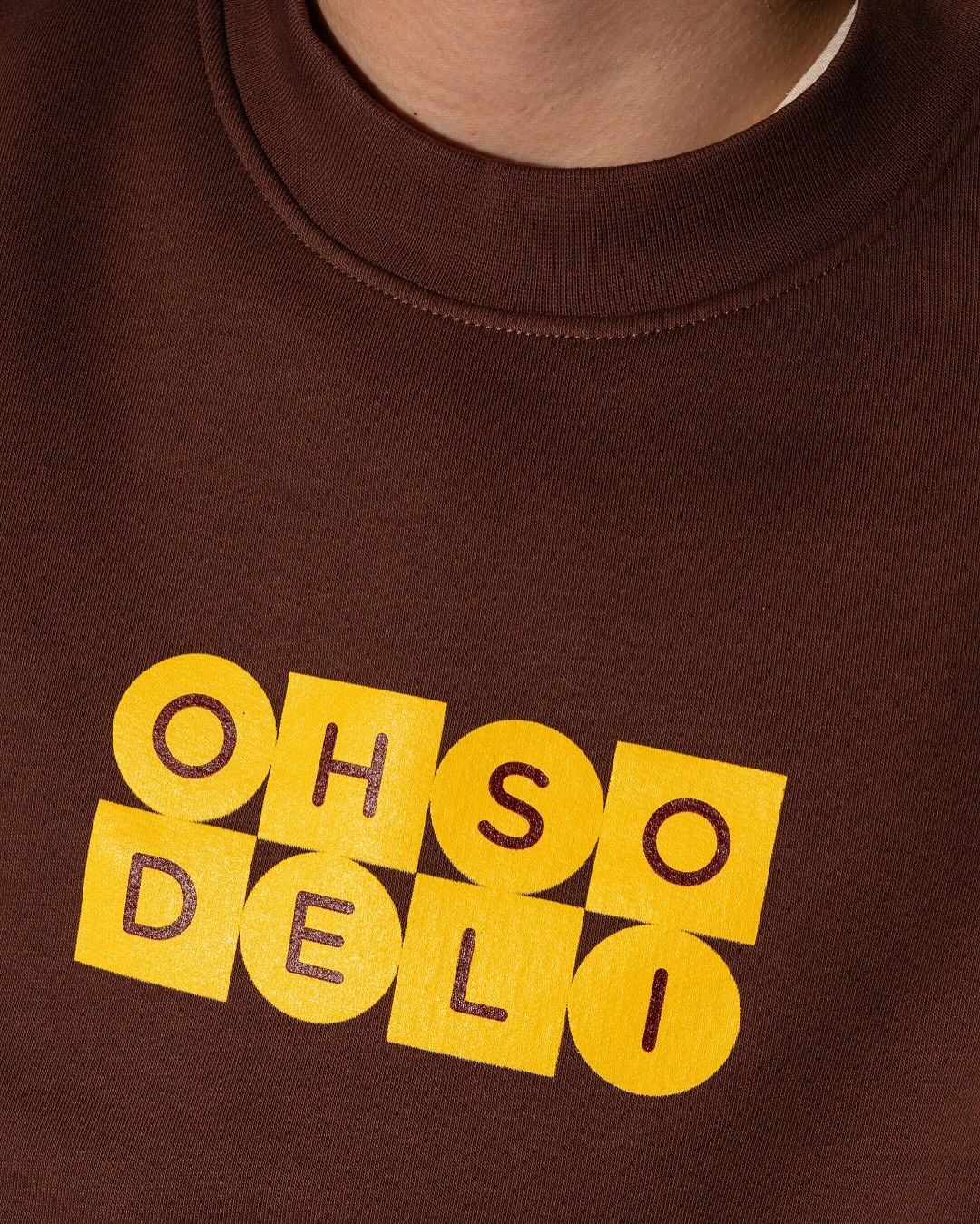 This is a minimalist graphic design featuring bold, capitalized text arranged in a grid pattern on a solid, earthy brown fabric. The design relies on high contrast between the bright yellow lettering and the dark background to create a clean, modern aesthetic.