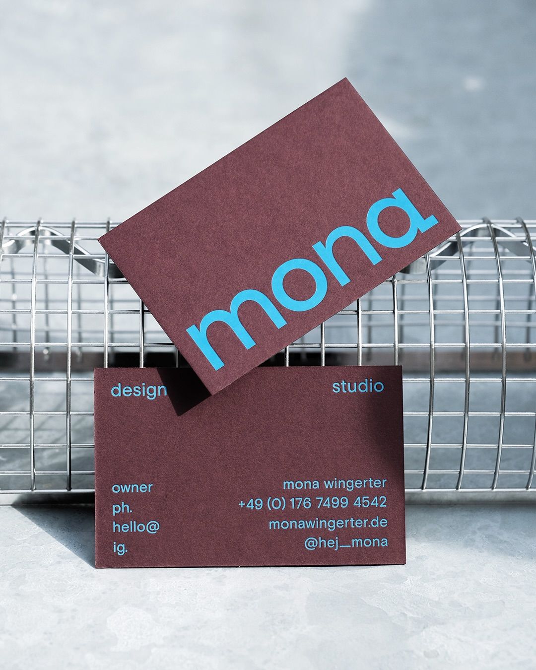 The image presents a clean, modern branding presentation featuring two overlapping rectangular cards with a deep maroon background and bright cyan text. The design is minimalist, relying on strong color contrast and simple typography to convey a professional and contemporary aesthetic.