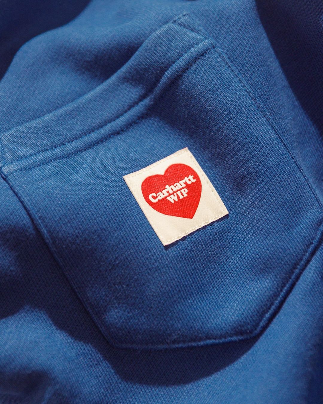 This image captures a close-up detail of a garment, focusing on the contrast between deep indigo fabric and a small, brightly colored branded patch. The visual language is clean and focused, utilizing negative space effectively to draw attention to the subtle textural quality and the intimate nature of the branding.