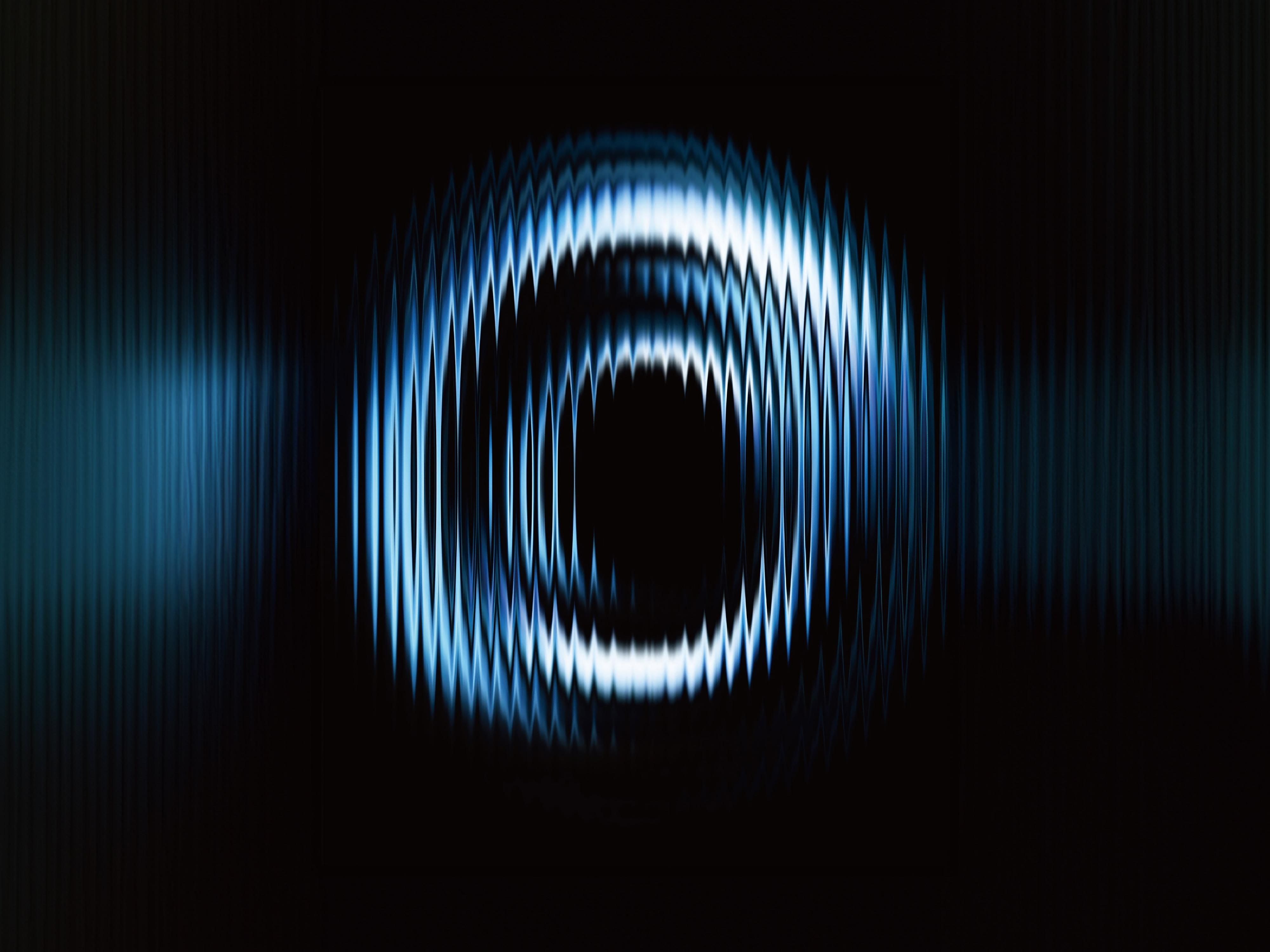 This image features a strong, concentric wave pattern emanating from a central dark void, creating a dynamic and abstract visual effect. The use of light blue tones against a deep black background suggests themes of sound, vibration, or energy.
