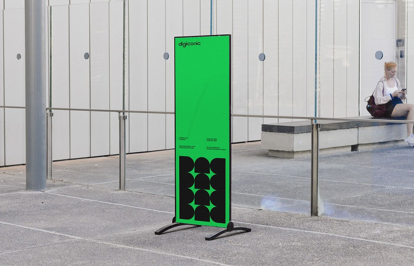 A striking minimalist public installation featuring a tall, neon green rectangular structure with geometric black circular patterns, positioned in a stark concrete plaza. The design employs bold color contrast and clean lines against an industrial architectural backdrop, creating a contemporary art or wayfinding piece that commands attention through simplicity and chromatic intensity.
