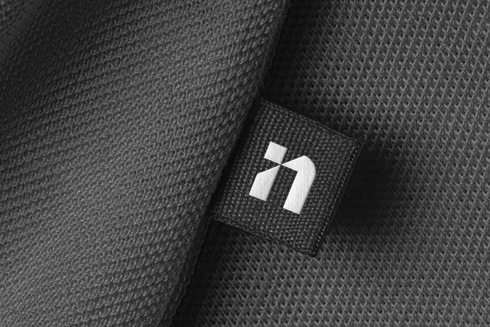 This image presents a high-contrast study of texture and minimalism, focusing on the interplay between a dark woven fabric and a subtle white branding tag. The visual language relies heavily on negative space and the tactile quality of the material to convey a sense of quiet sophistication and refined detail.