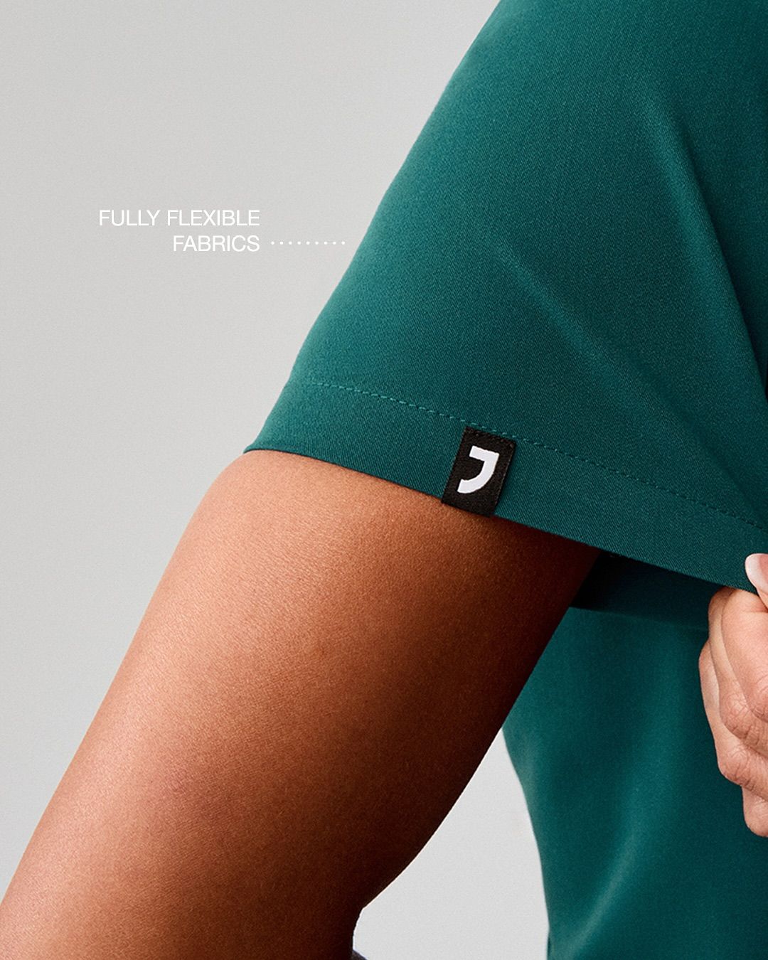 This image showcases a close-up view of a deep teal garment, emphasizing the flexibility and texture of the fabric. The visual language is clean and functional, highlighting a small, minimalist black logo detail against the rich color of the textile.